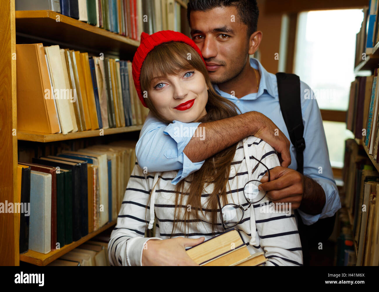 Jeune couple d'étudiants choisissant de livres entre les étagères de la bibliothèque Banque D'Images