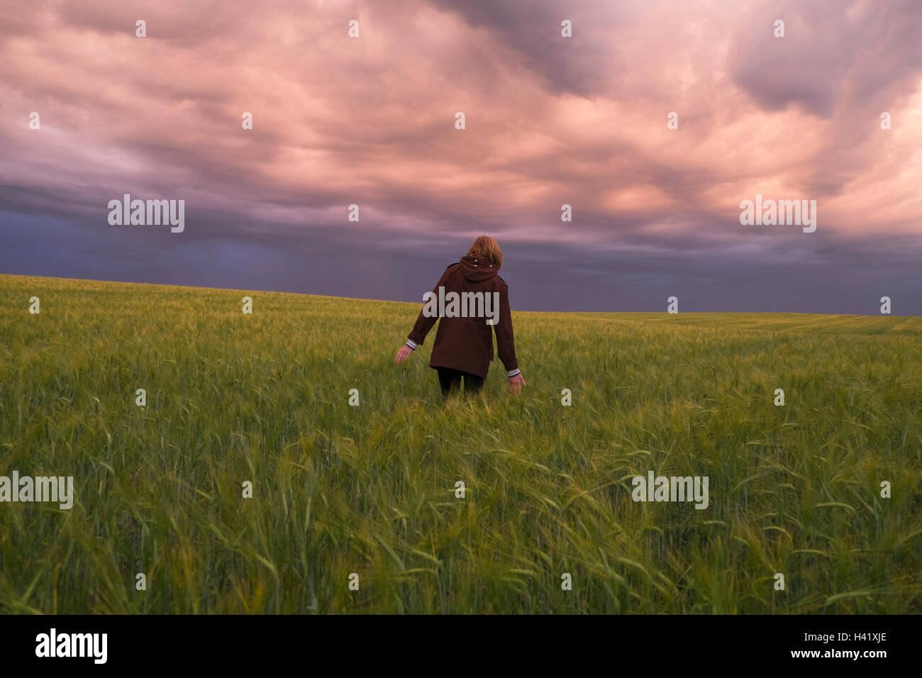 Storm clouds over Caucasian woman walking in field of tall grass Banque D'Images