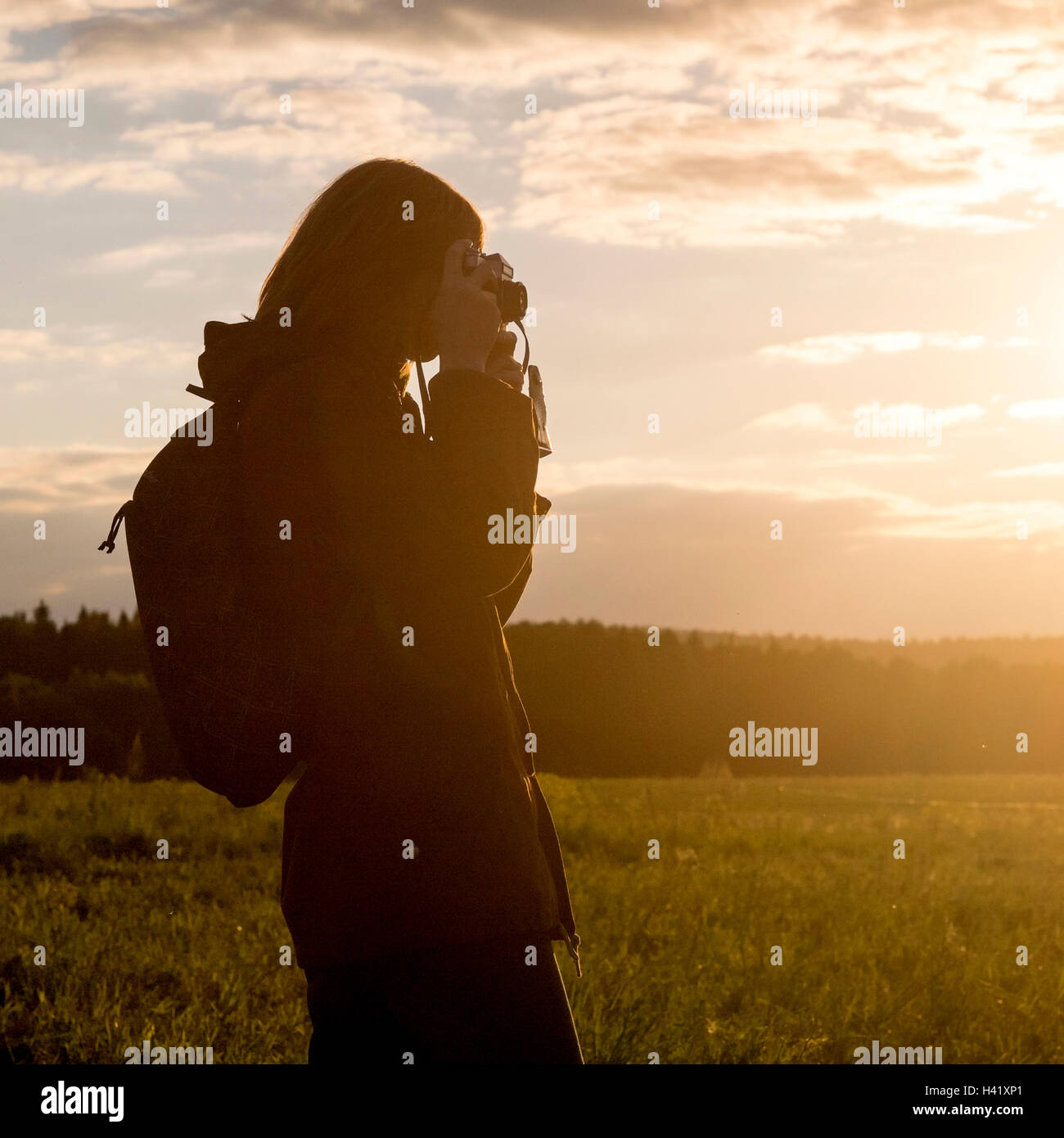 Caucasian woman photographing avec caméra dans le champ au coucher du soleil Banque D'Images