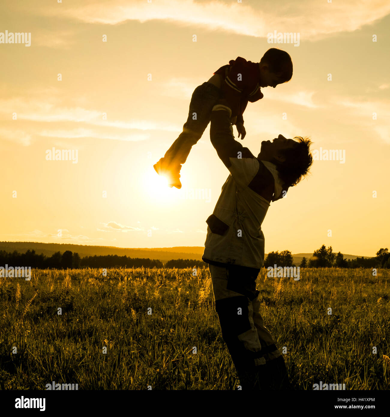 Mari man lifting fils dans le champ au coucher du soleil Banque D'Images