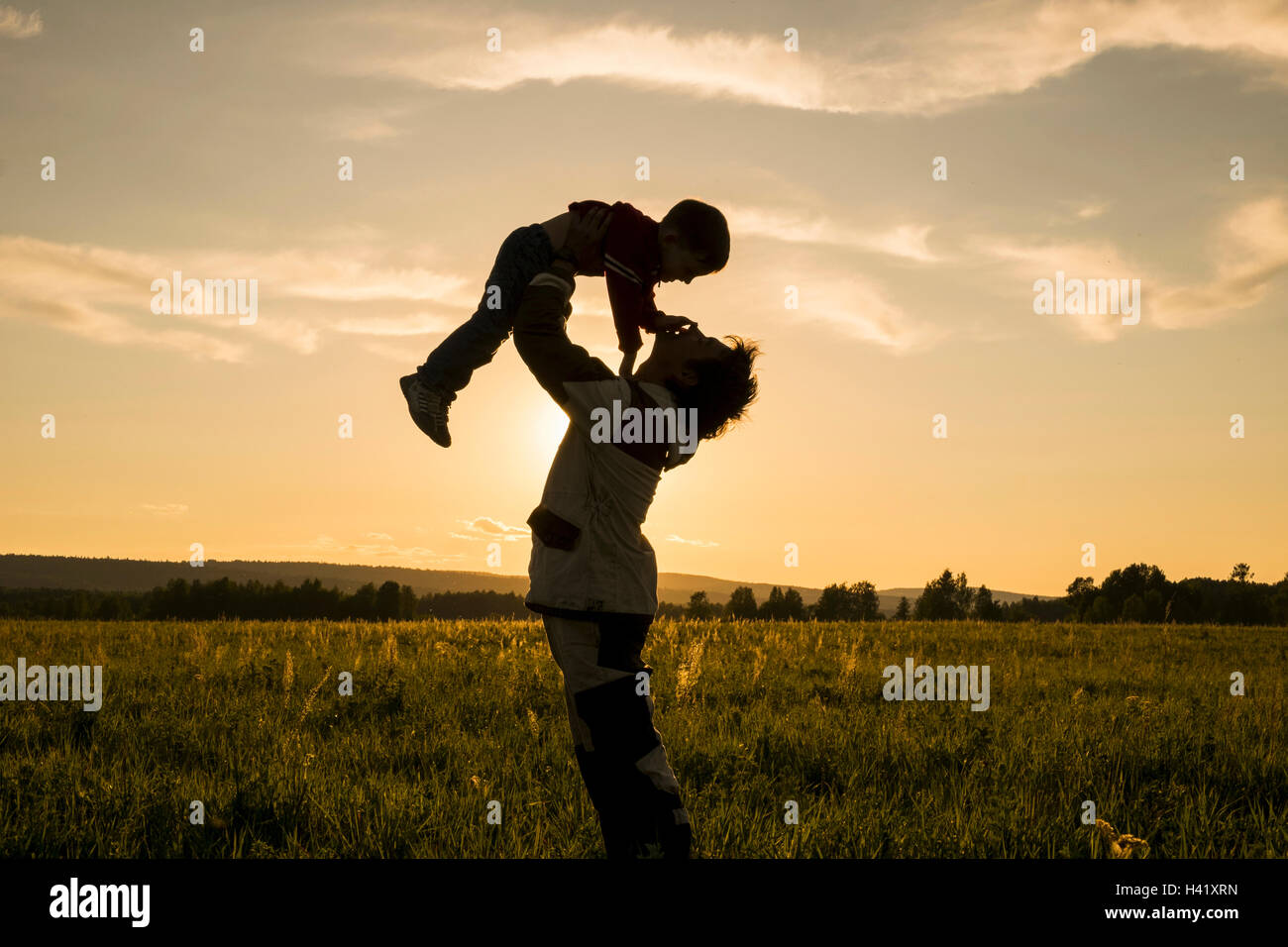 Mari man lifting fils dans le champ au coucher du soleil Banque D'Images