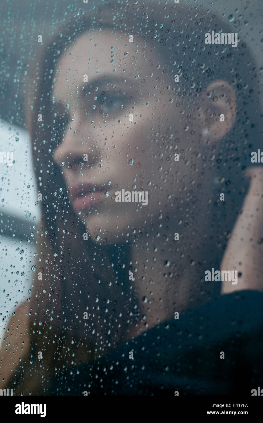 Femme regardant à travers une fenêtre des pluies Banque D'Images