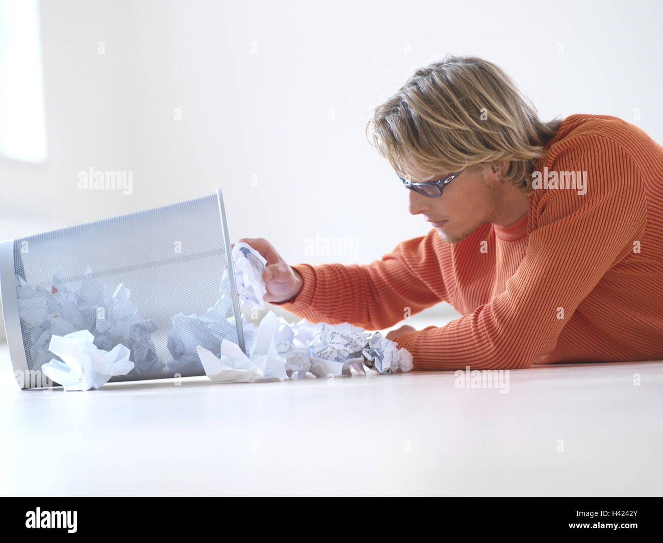 L'homme, corbeille, parcourir, étage, se trouvent les jeunes, blonde, lunettes, position abdominale, tendu, de concentrés, d'intérêts curieusement, au sérieux, les poubelles, les déchets de papier, creuser, fouiller dans, vous pouvez, choisir, documents, bases, de lettres, de documents, froisse, lo Banque D'Images