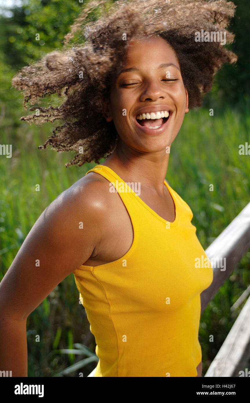 Jeune femme, rire, la peau sombre, pont, heureux, demi-portrait, les non-blancs, boucles, aux cheveux bruns, l'été, le soleil, profiter, loisirs, vacances, drôlement la vie, la joie, le plaisir, la joie, l'insouciance, de désinvolture, exhilarates, heureux, motion, top, débardeur, résumé, jaune, fondu, de la jeunesse, amuse, vivacité, vitalité, impulsivement, positivement, l'humeur, de transmission, de naturel, à l'extérieur de la jetée en bois, stand, mode de vie, Banque D'Images