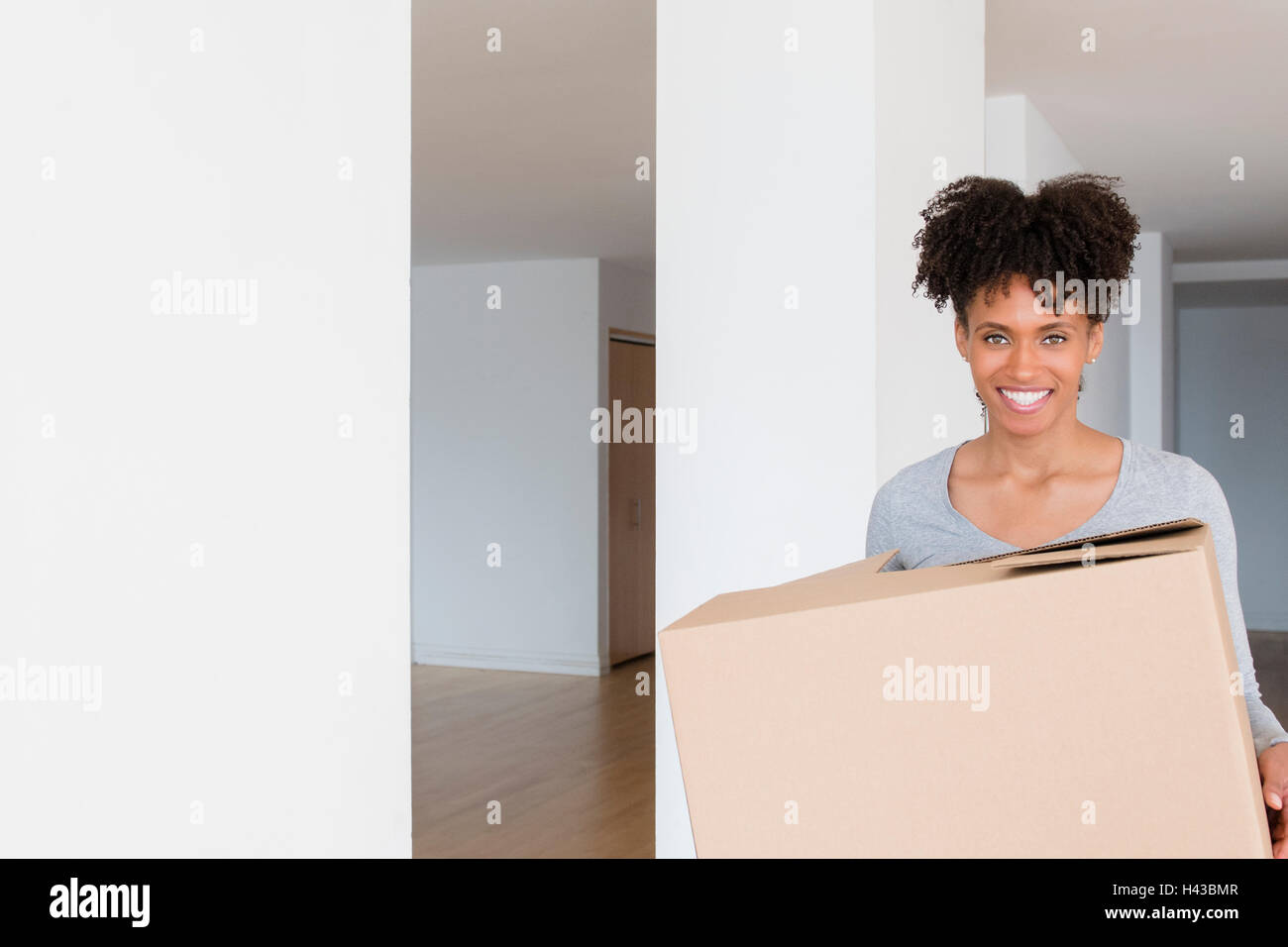 Black woman carrying cardboard box in empty apartment Banque D'Images