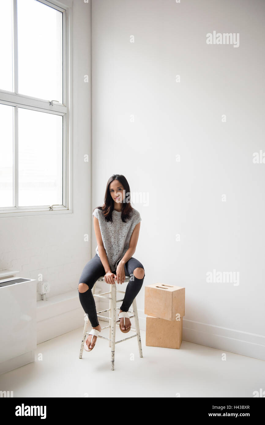 Mixed Race woman sitting on stool en corner Banque D'Images