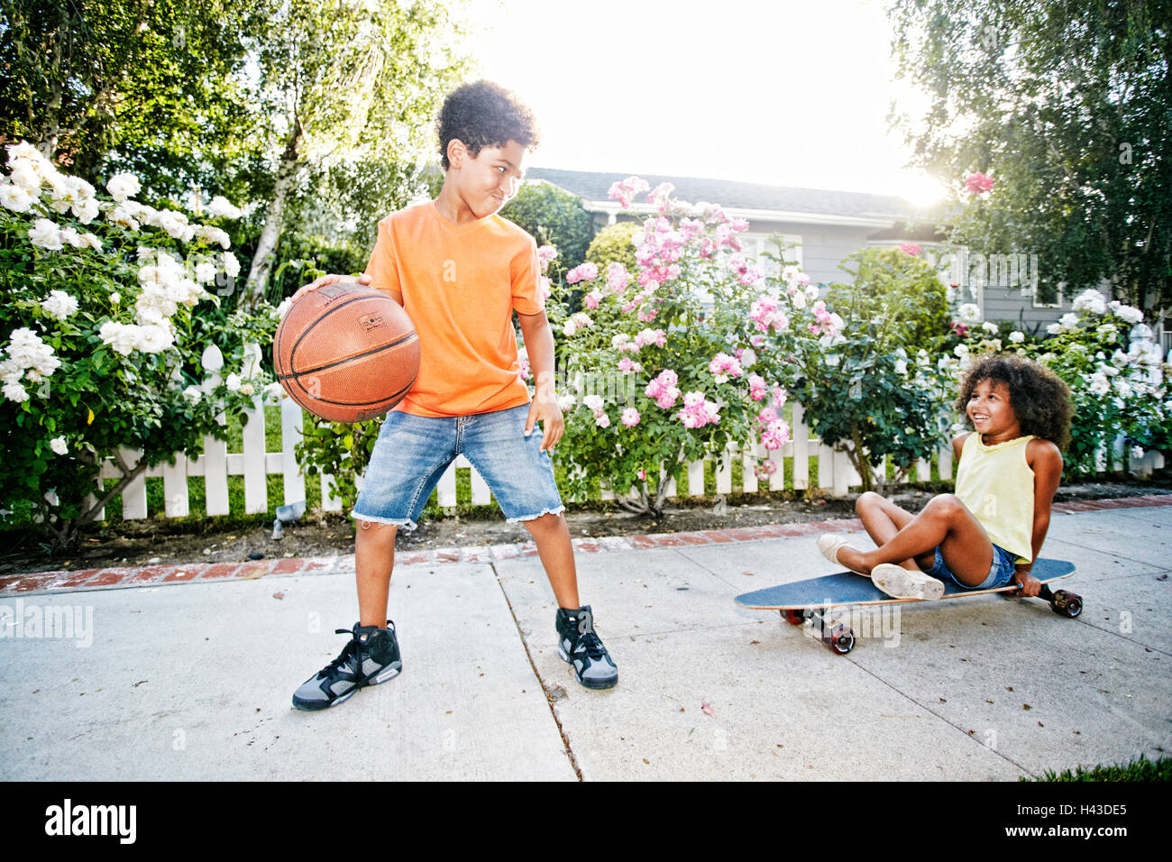 Mixed Race girl sur planche regardant frère dribbling basketball Banque D'Images