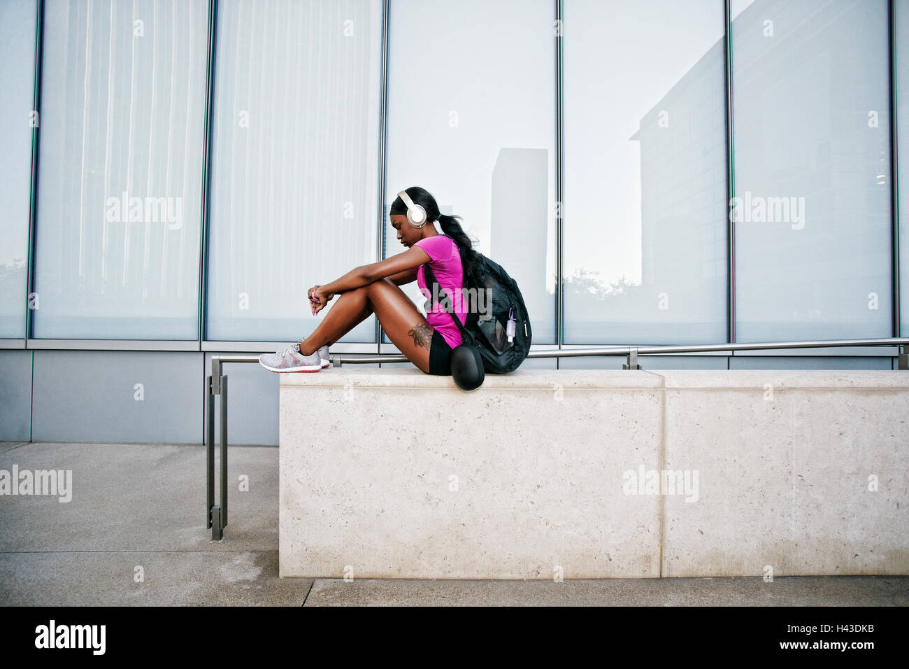 Black woman sitting on wall urbain listening to headphones Banque D'Images