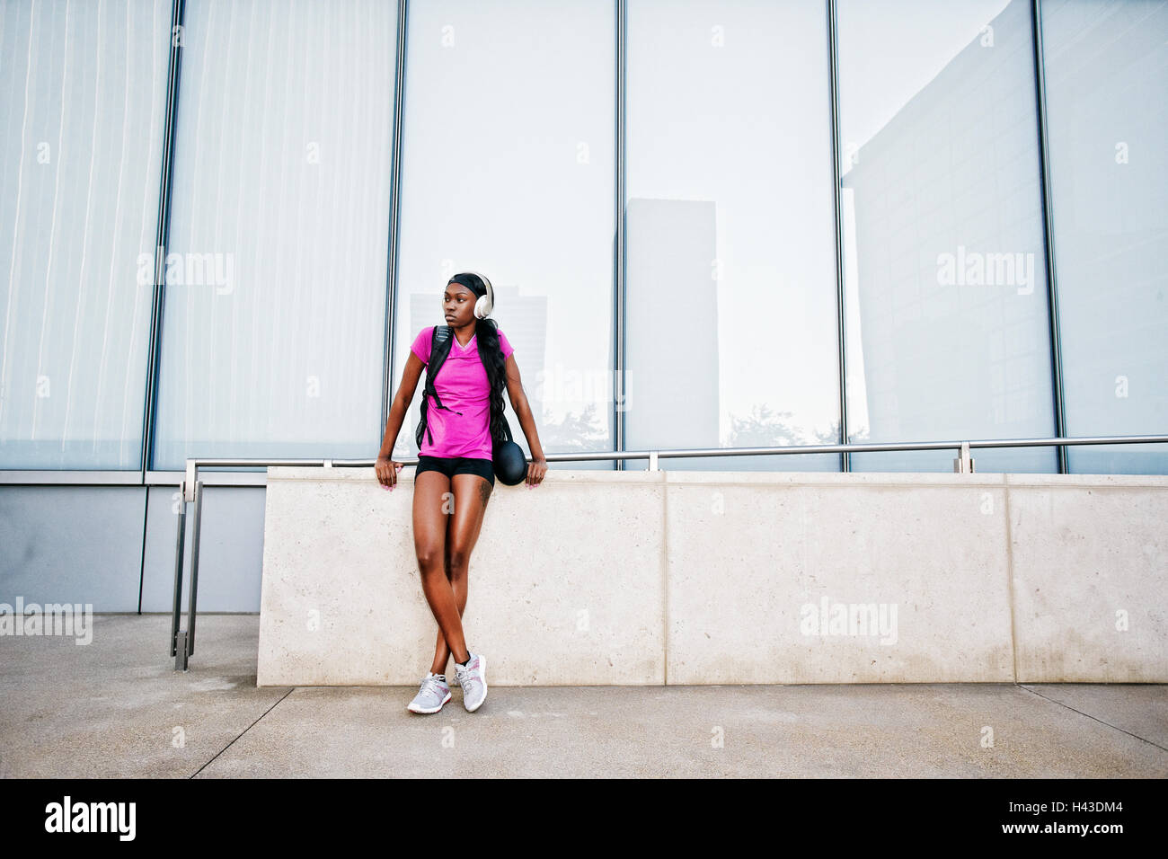 Black woman leaning on urban wall listening to headphones Banque D'Images