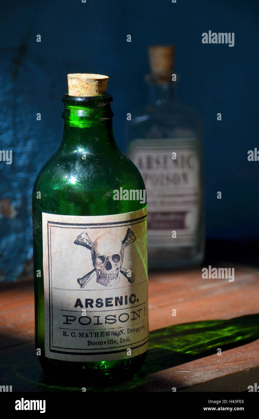 Ancien verre vert bouteille étiquetée avec poison de l'arsenic et du crâne et les os se trouve sur une étagère. Une autre bouteille de poison se trouve derrière. Banque D'Images