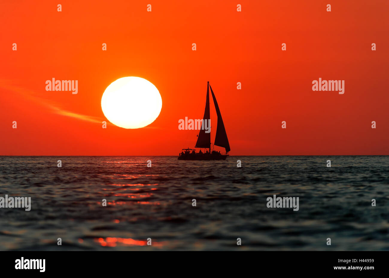 Coucher du soleil est un voilier avec équipage à bord du bateau qui se profile la voile le long de l'océan de l'eau avec un bain de soleil blanc dans le soleil rouge Banque D'Images