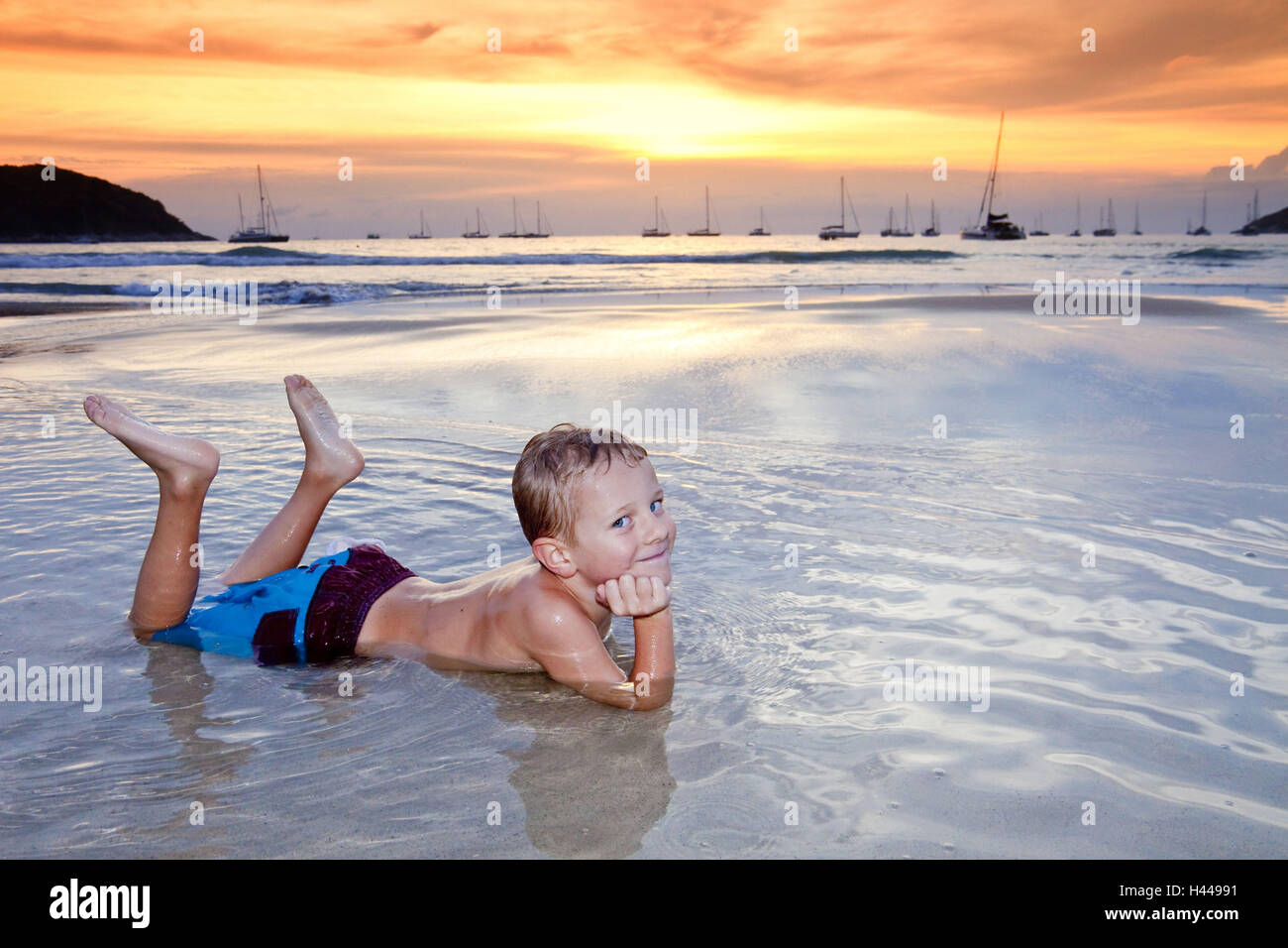 L'île de Thaïlande, Phuket, Nai Harn Beach, garçon, de l'eau, faible profondeur, mensonge, le coucher du soleil, Banque D'Images