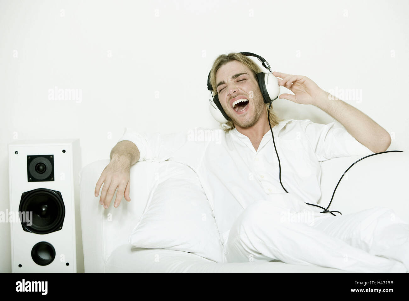 L'homme, jeunes, écouteurs, entendre la musique, chanter, les gens, blonde, poil long, 3-jours non rasé, barbe, loisirs, passe-temps, de musique, inscrivez-vous dans le chant, d'un salon, de la table, s'asseoir, haut-parleur, blanc, Banque D'Images