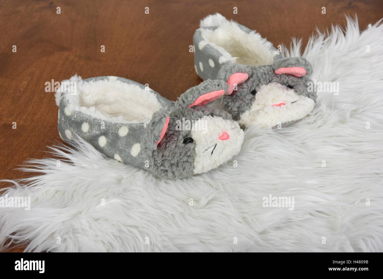 Paire de chaussons lapin fourrure blanche sur un tapis et plancher de bois Banque D'Images