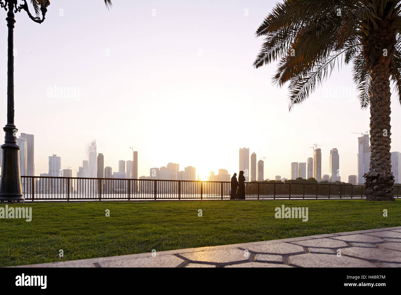 Habitants flâner au coucher du soleil en corniche Street, Skyline, contrejour, Emirat Sharjah, Émirats arabes unis, péninsule arabique, le Moyen-Orient, l'Asie, Banque D'Images
