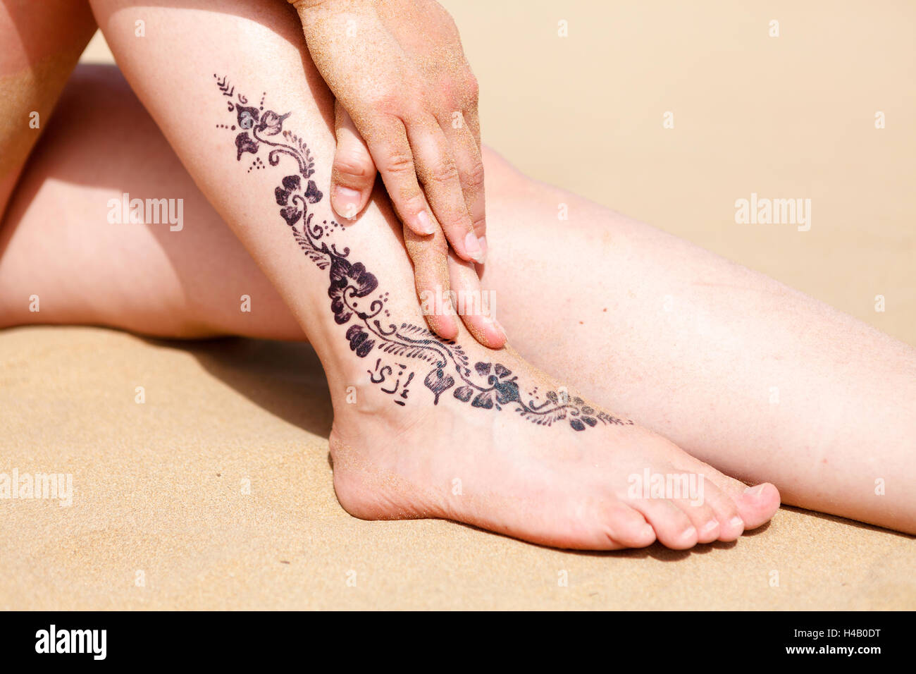 Tatouage au henné sur la jambe de la femme contre une plage de sable Banque D'Images