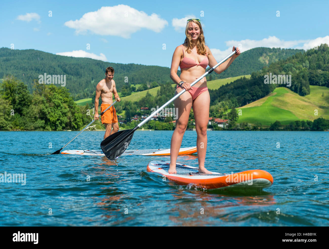 Jeune homme et femme sur paddle boards, à l'aide de stand-up paddles, lac Schliersee, Haute-Bavière, Bayern, Allemagne Banque D'Images