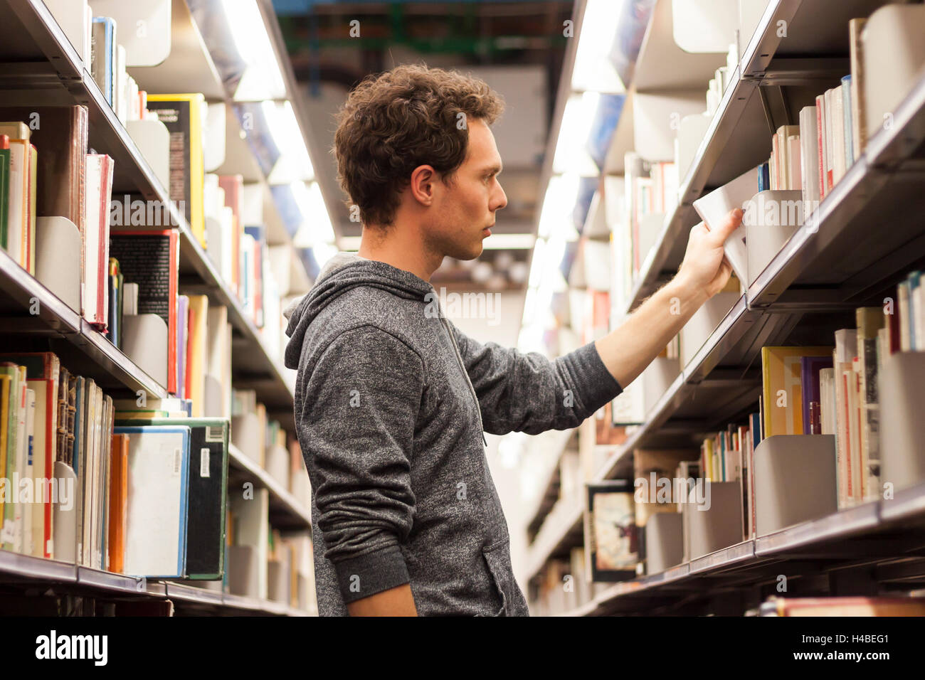 Young male student la sélection d'un livre d'une étagère de bibliothèque, l'école secondaire Banque D'Images