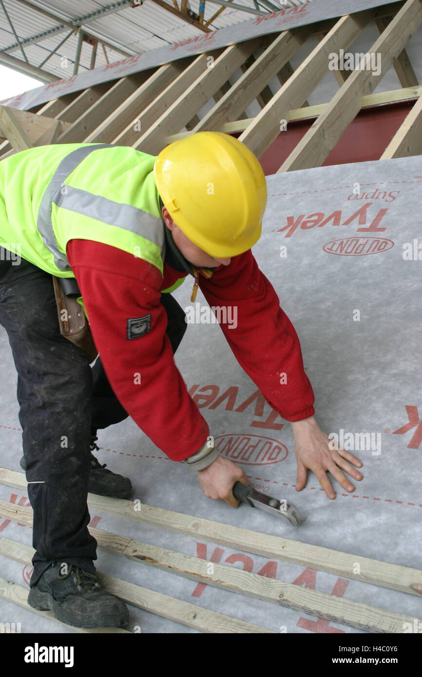 Un couvreur fixe une nouvelle membrane imperméable pour le toit d'une maison en rénovation Banque D'Images