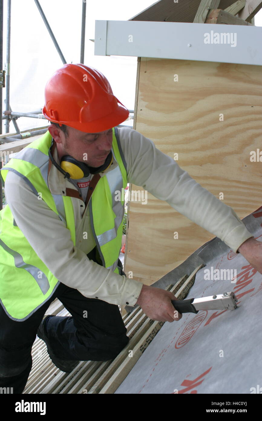 Un couvreur fixe une nouvelle membrane imperméable pour le toit d'une maison en rénovation Banque D'Images
