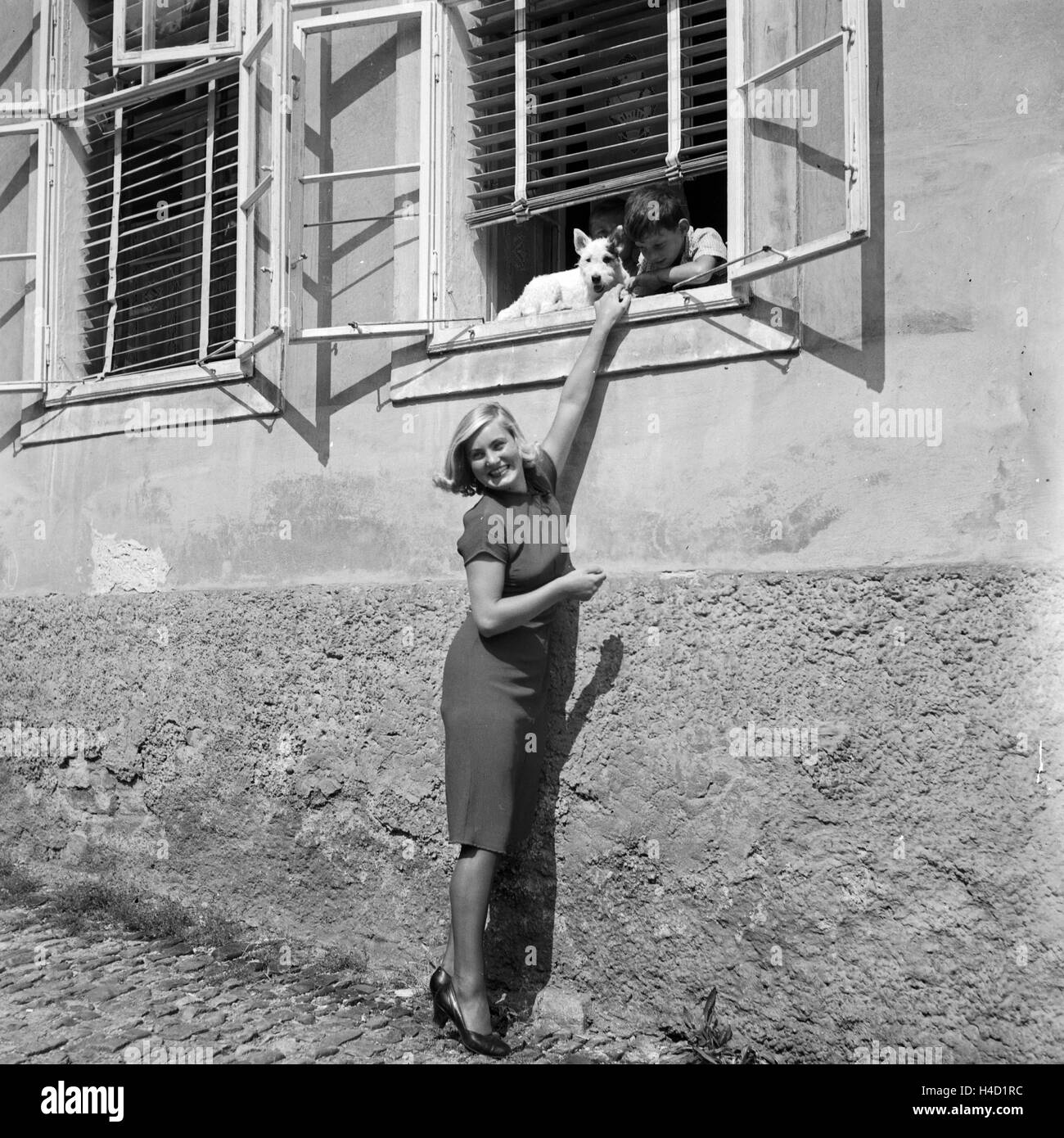 Eine junge Frau unterhält sich am Fenster mit einem kleinen Jungen und seinem Hund, Deutschland 1930er Jahre. Une jeune femme avec un garçon et son chien dans une fenêtre, l'Allemagne des années 1930. Banque D'Images