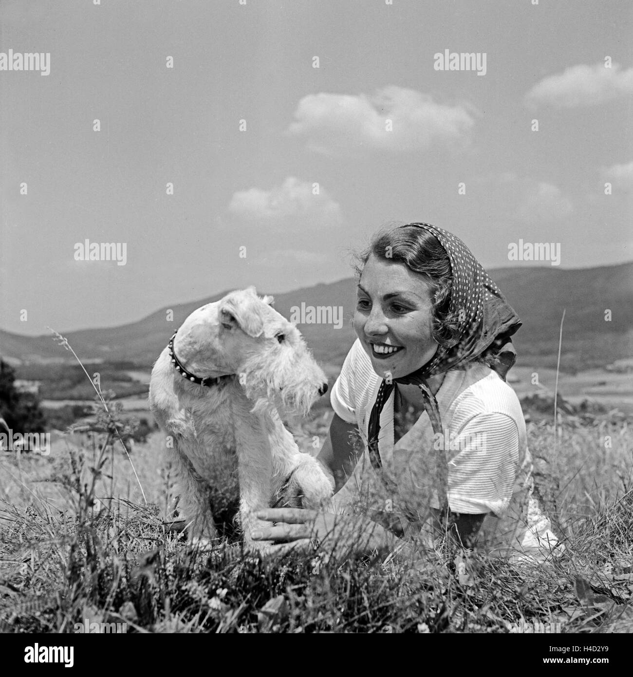 Eine junge Frau sitzt mit einem Foxterrier in einer Wiese, Deutschland 1930 er Jahre. Une jeune femme assise dans une pelouse avec son chiot fox terrier, Allemagne 1930. Banque D'Images