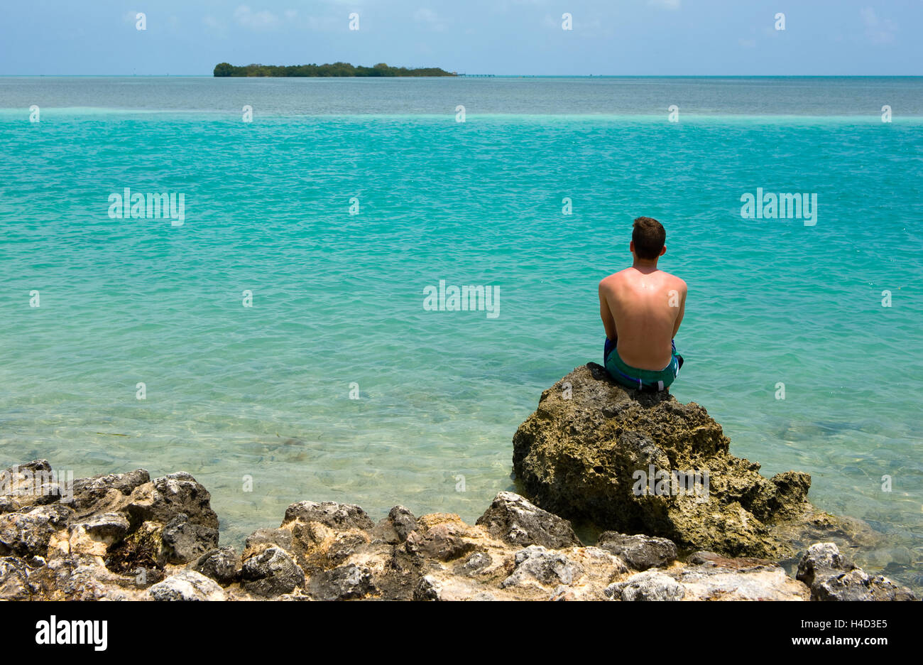 Un adolescent est assis sur un rocher sur une plage de la Florida Keys Banque D'Images