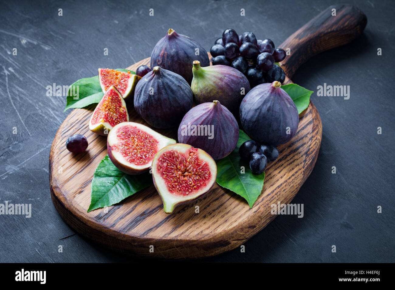 Plateau à fruits : figues fraîches et les raisins noirs 'Isabella' sur planche à découper en bois. L'horizontale Banque D'Images