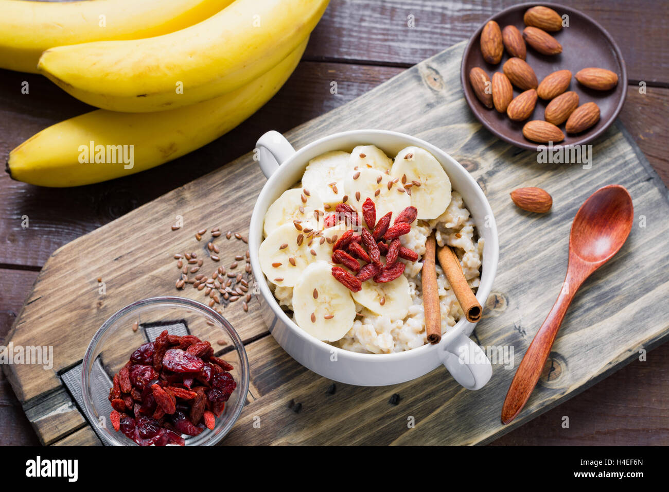 Gruau d'avoine avec bananes, cannelle, baies de goji secs et graines de lin sur la planche à découper en bois. Une alimentation saine, bonne hygiène de vie Banque D'Images