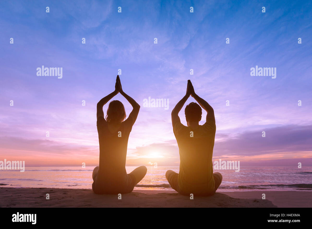Deux jeunes adultes en faisant une formation de yoga à la plage pendant le coucher du soleil pour la méditation et la vie saine Banque D'Images