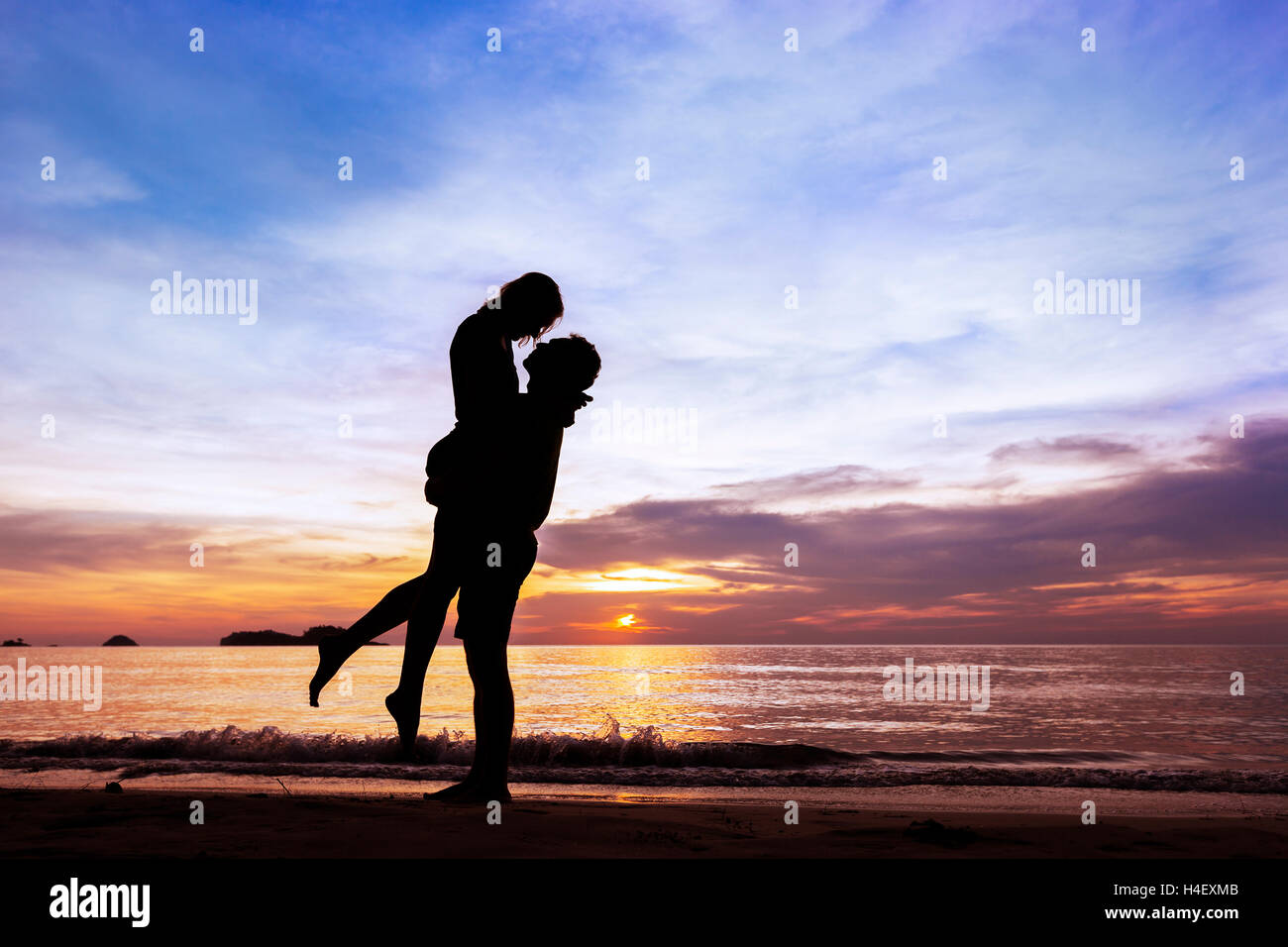 Silhouette d'heureux couple sur Paradise beach au coucher du soleil, l'homme de prendre la jeune fille dans ses bras Banque D'Images