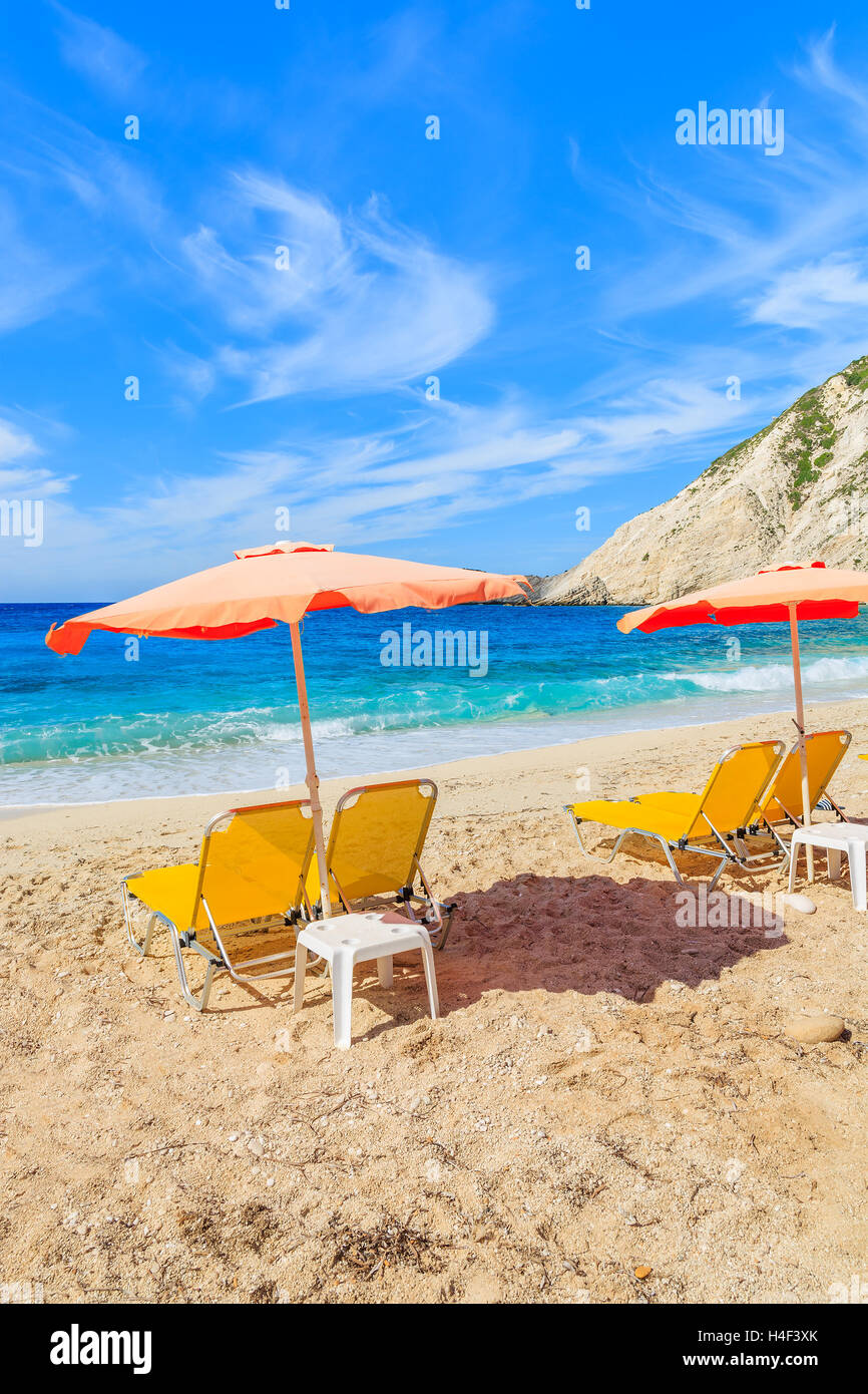 Chaises longues jaune avec un parapluie rouge sur la belle plage de Petani, l'île de Céphalonie, Grèce Banque D'Images