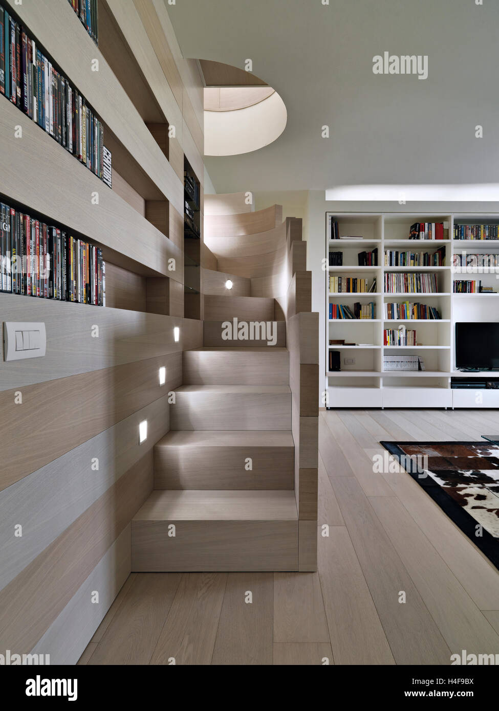 Salon moderne en premier plan l'escalier en bois donnant sur la grande bibliothèque dont le sol est en bois Banque D'Images