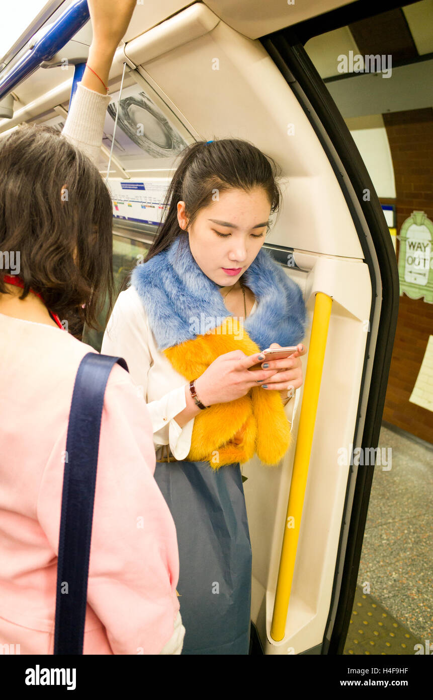Young Asian woman using smartphone dans le métro de Londres, Angleterre, RU Banque D'Images