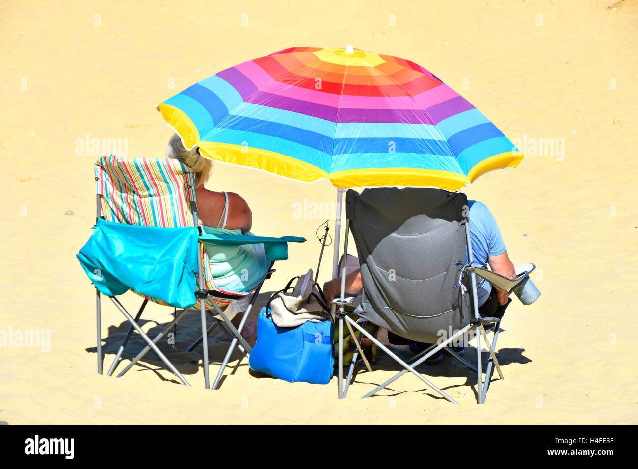 Couple mature parasol coloré de plage de détente dans les chaises pliantes sur le sable de vacances plage ombre de soleil chaud d'été Ryde Isle of Wight Royaume-Uni Banque D'Images