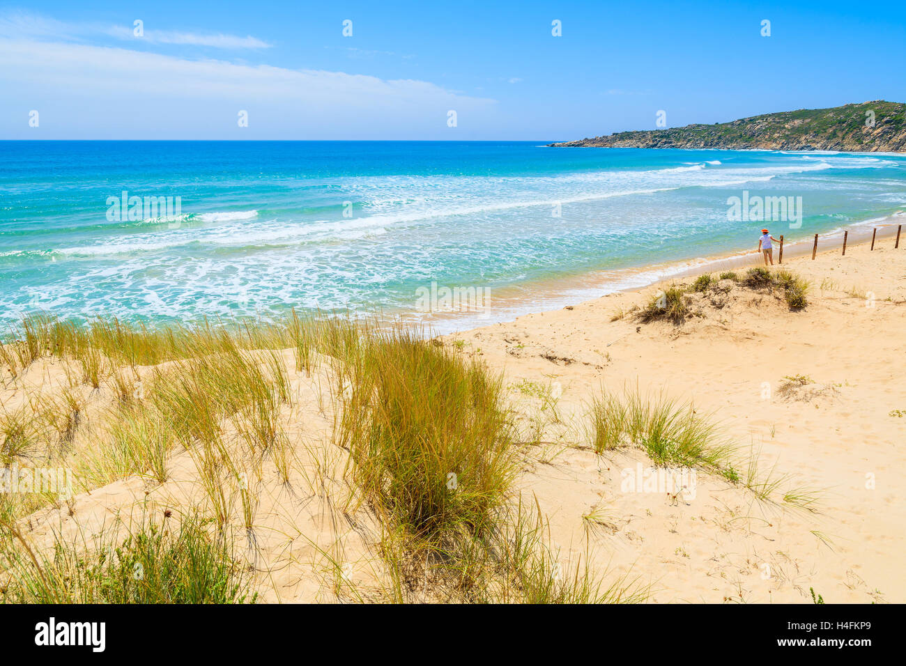 L'herbe sur dune de sable à Chia et jeune femme debout dans la distance contre une clôture, l'île de la Sardaigne, Italie Banque D'Images