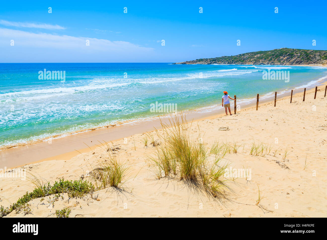 L'herbe sur dune de sable à Chia et jeune femme debout dans la distance contre une clôture, l'île de la Sardaigne, Italie Banque D'Images