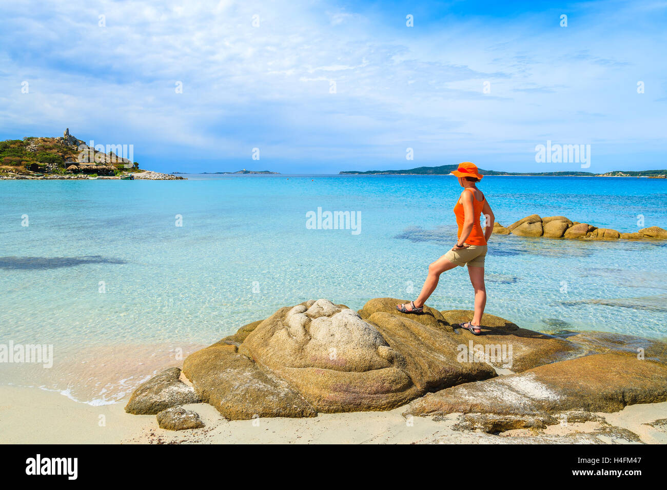 Jeune femme debout touristiques sur un rocher et regarder la mer turquoise clair comme de l'eau à la plage de Punta Molentis, Sardaigne, île, Italie Banque D'Images