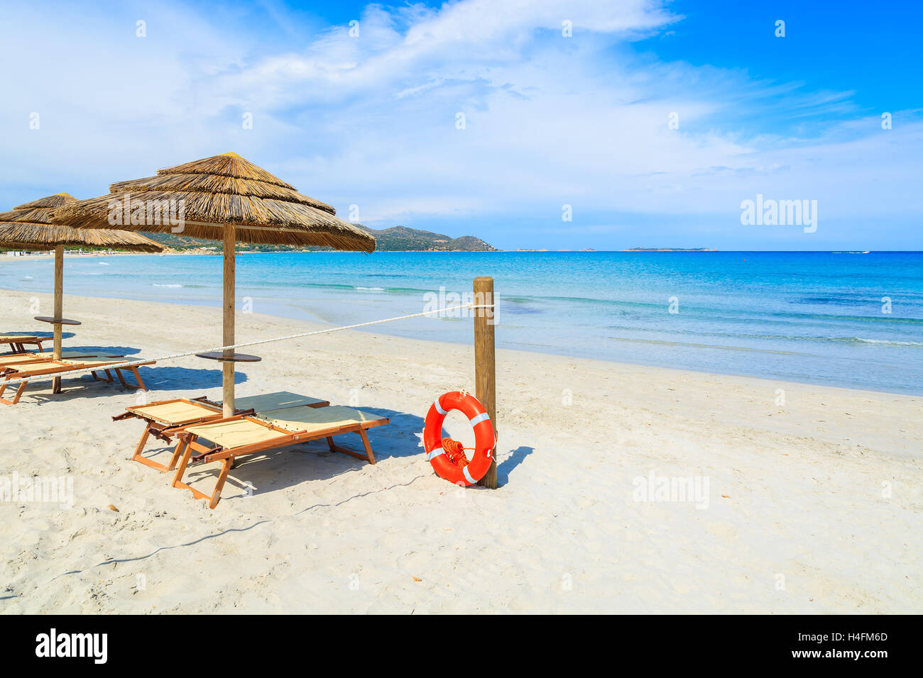 Des chaises longues avec parasols et rouge bague la vie sur un poteau en bois sur une plage de sable blanc, Porto Giunco Bay, île de Sardaigne, Italie Banque D'Images