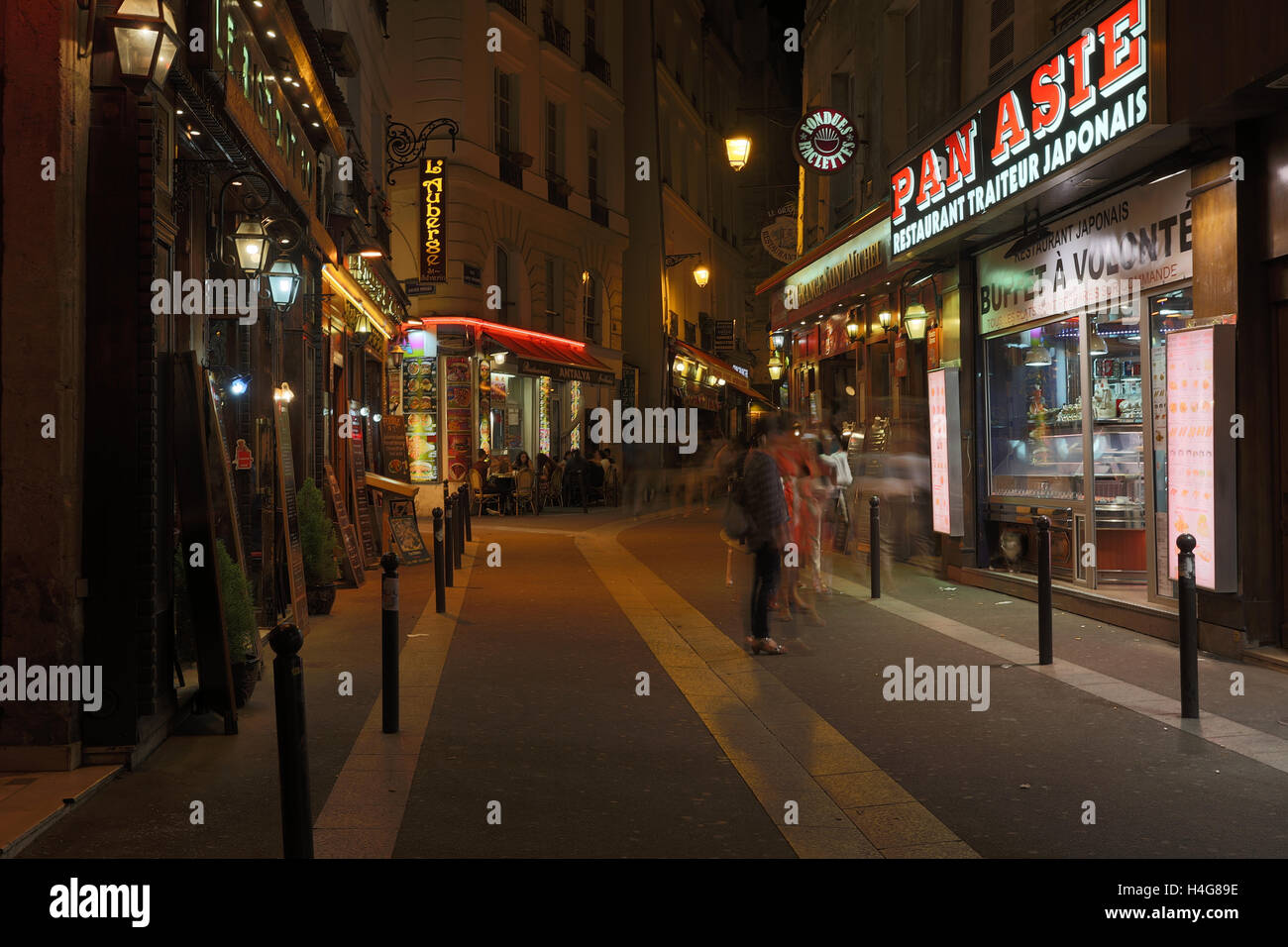 PARIS, FRANCE - 13ème Août 2016 : une vue dans une rue de Paris la nuit montrant le mouvement flou de personnes et de restaurants, cafés et autres commerces Banque D'Images
