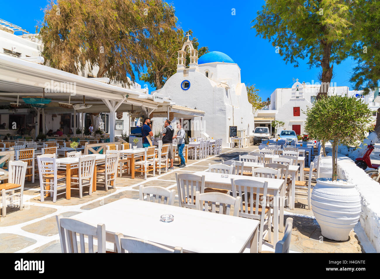 La ville de Mykonos, Grèce - 16 MAI 2016 : hommes parler grec dans une taverne typique avec des chaises et tables en face d'une église blanche dans mon Banque D'Images