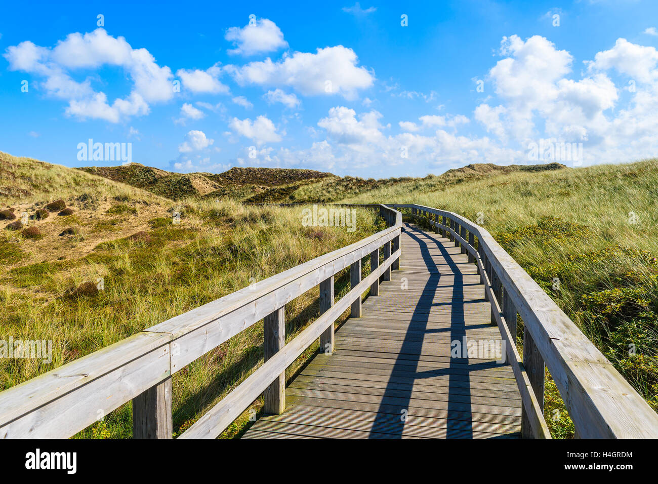 Passerelle en bois de la plage entre les dunes de sable et de ciel bleu ensoleillé avec des nuages blancs, l'île de Sylt, Allemagne Banque D'Images