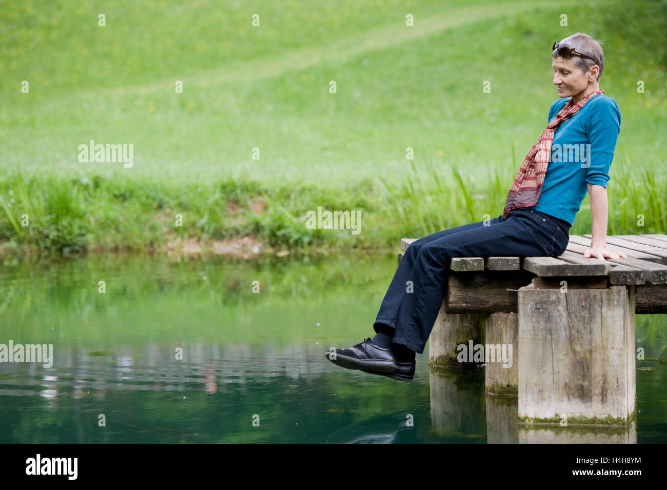 Dame, 60 ans, assis sur un ponton de l'étang Banque D'Images