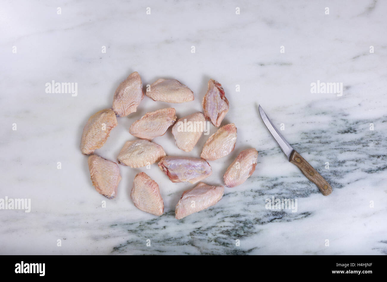Vue aérienne d'ailes de poulet crues et couteau de cuisine de comptoir en pierre de marbre naturel Banque D'Images
