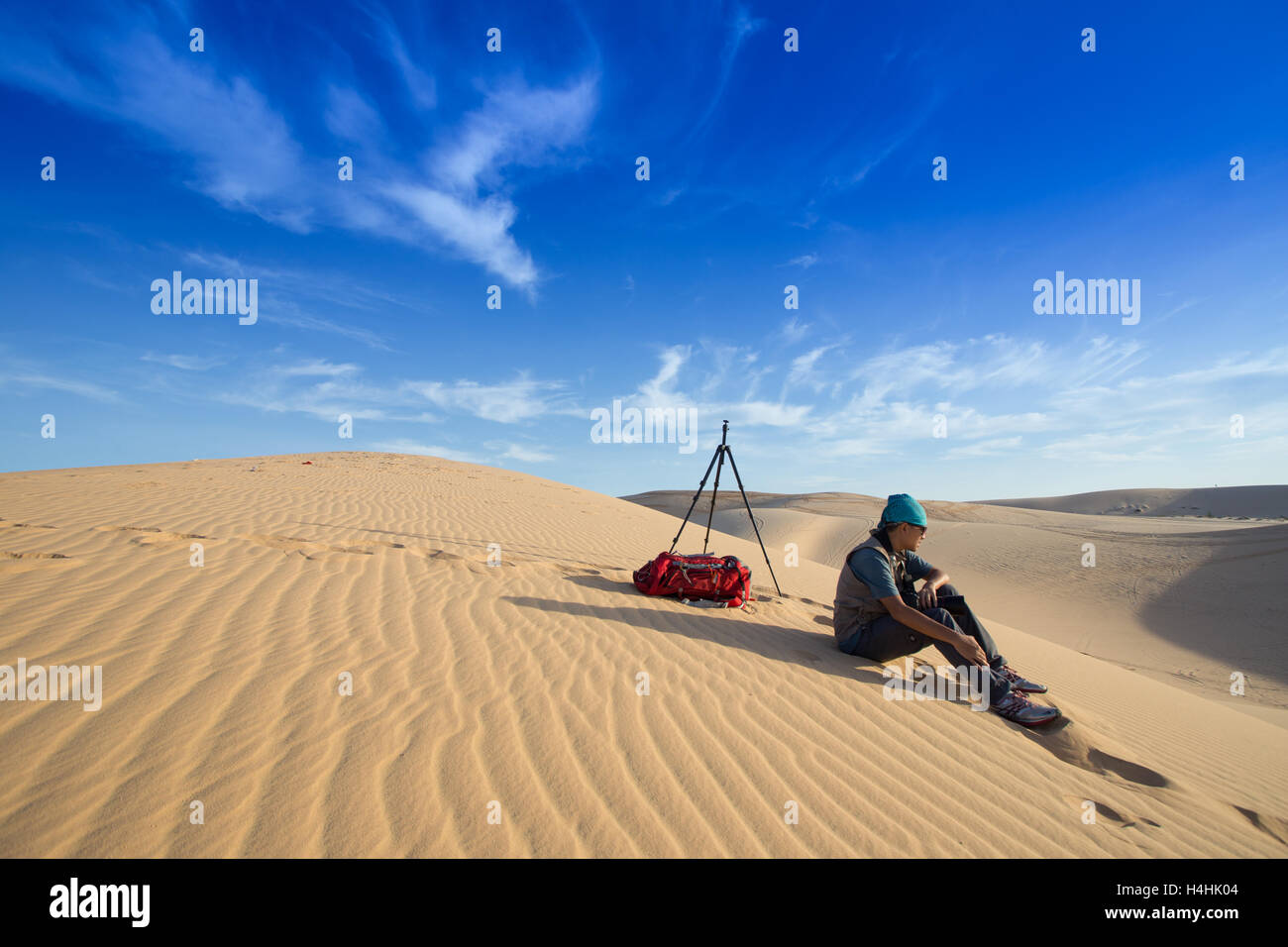 Photographe homme voyageant avec son sac à dos de l'appareil photo et le trépied assis sur les dunes de sable blanc au désert Muine, Phan Thiet, Vietnam Banque D'Images