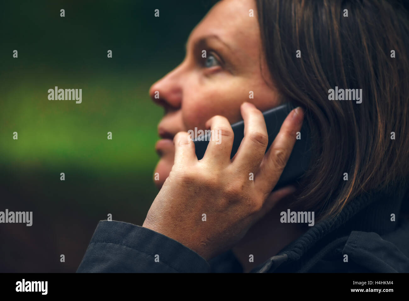 Femme avec sérieux talking on mobile phone in park, dramatique du voyant à travers la cime des arbres et de tomber sur son visage Banque D'Images