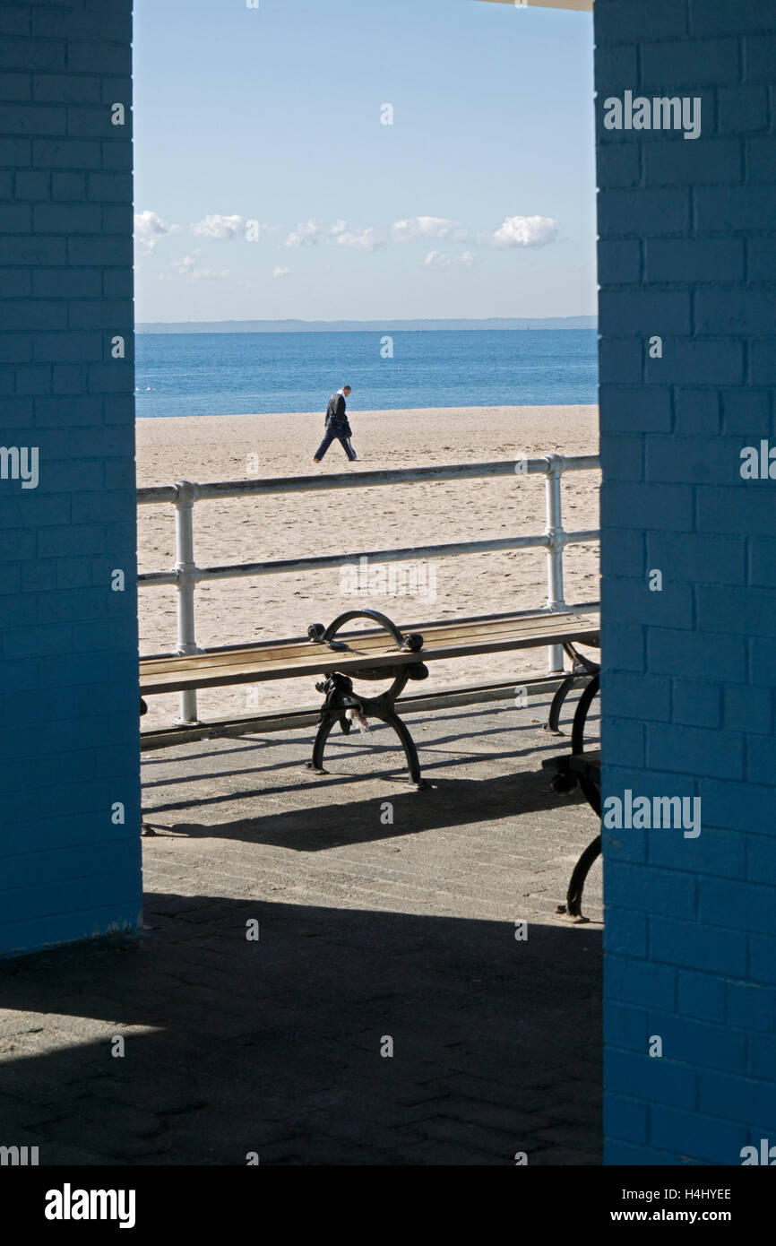 Un homme solitaire marche sur une étendue de plage isolée à Coney Island, Brooklyn, New York Banque D'Images