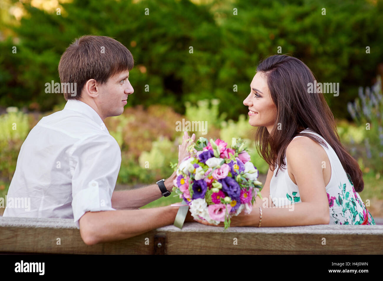 Amour couple sitting on bench avec bouquet de fleurs Banque D'Images