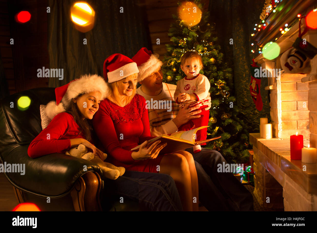 Famille - papa, maman avec filles assis sur un canapé et cheminée près de reading book Banque D'Images