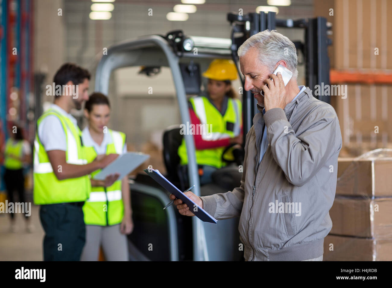 Warehouse Manager talking on mobile phone et la tenue d'un presse-papiers Banque D'Images